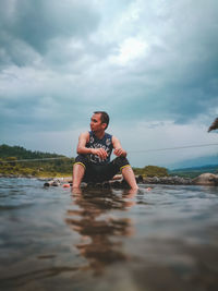 Man sitting in sea against sky