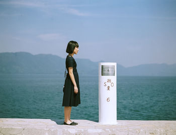 Woman standing by bollard on retaining wall at seaside