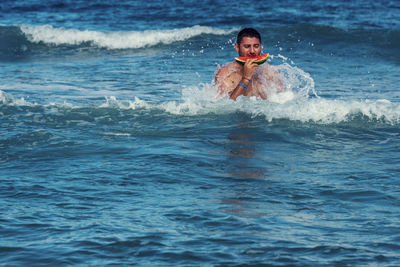 Man eating watermelon while swimming in sea