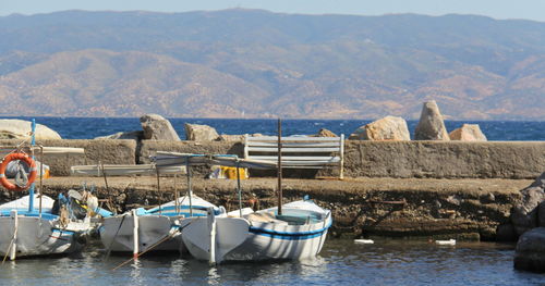 Boats moored on sea by mountains against sky