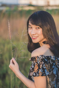 Portrait of young woman holding grass while standing on field