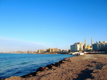 Sea and buildings against clear blue sky