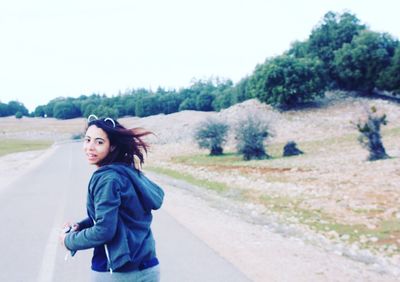 Portrait of young woman standing on road against trees