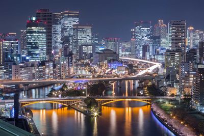 Illuminated bridge over river amidst buildings in city at night