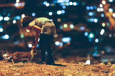 Girl touching cat on field at night