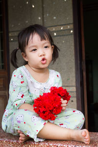 Cute girl holding red flowers while sitting on retaining wall