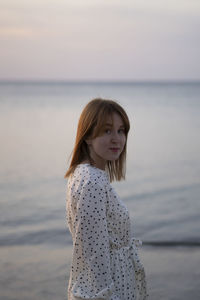 Young woman standing at beach against sky during sunset