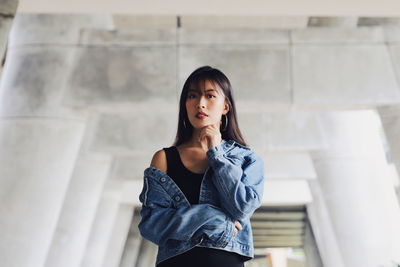 Fashionable young woman wearing denim jacket while standing below bridge