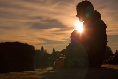 Silhouette woman sitting with daughter against sky during sunset