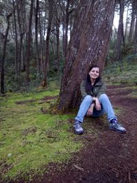 Portrait of young man sitting on tree trunk in forest