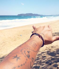 Cropped tattooed hand of woman gesturing at beach