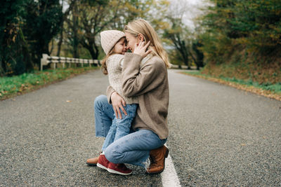 A tender mother hugs her little daughter while squatting outdoors