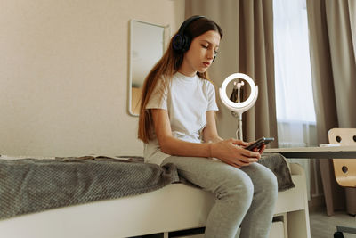 Generation z girl in headphones with a smartphone sits on the bed