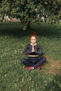 Young attractive girl in sports tight clothes doing exercises in the park among green foliage