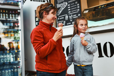 Mother and her daughter eating ice cream sitting on a step in front of food truck during vacations