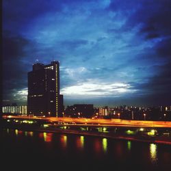 Illuminated buildings by river against sky at night