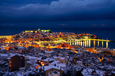 High angle view of illuminated city by sea against sky