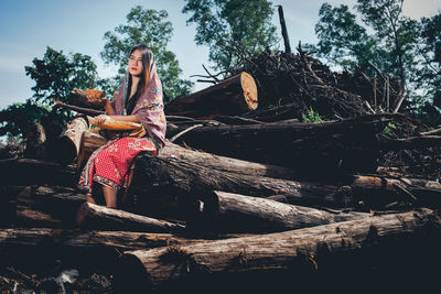 Thoughtful young woman sitting on logs in forest