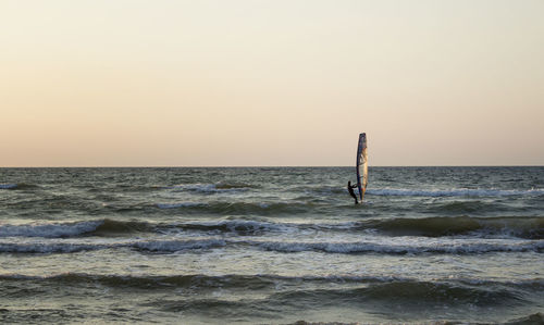 Person windsurfing on sea against sky during sunset