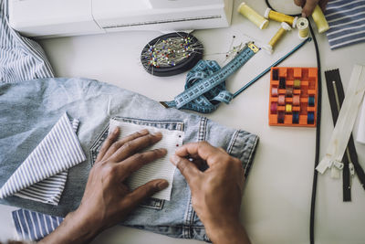 Directly above view of fashion designer pinning fabric on jeans pocket at workshop