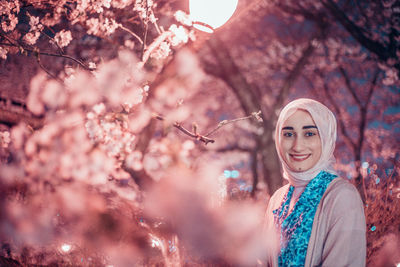 Portrait of a smiling young woman standing by cherry blossom