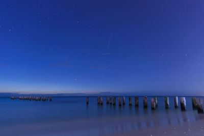 Wooden posts in sea against sky at night