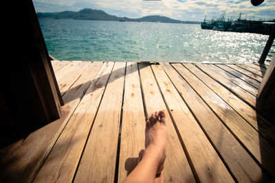 Low section of woman sitting on wooden floor of a bungalow with the view of the sea