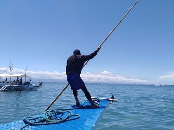 Man fishing in sea against blue sky