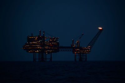 Illuminated crane in sea against clear sky at night