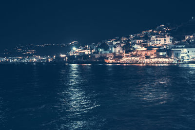 Illuminated buildings by sea against sky at night