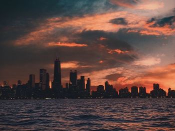 Sea by buildings against sky during sunset