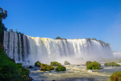Scenic view of waterfall against blue sky