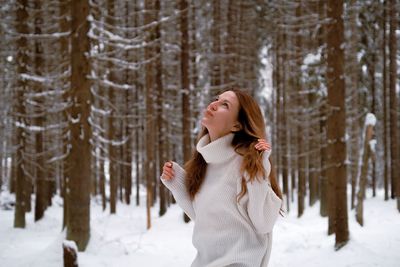 Side view of young woman standing in forest during winter