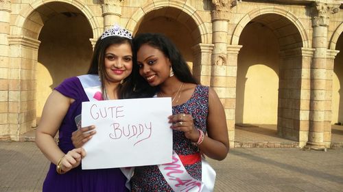 Portrait of smiling females showing placard while standing against building