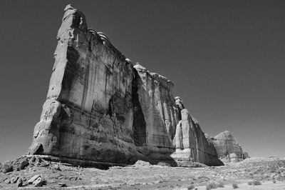 Low angle view of impressive desert rock formation on land against clear sky in black and white