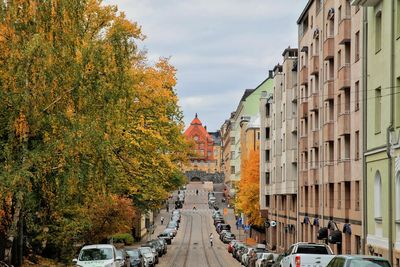 Cars on road amidst buildings against sky during autumn