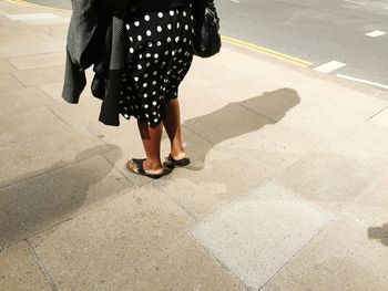 Low section of woman wearing dress standing on sidewalk