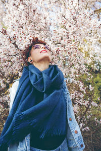 Beautiful young woman looking up while standing against cherry tree