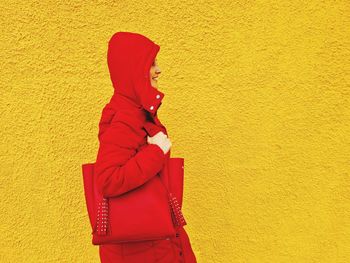 Woman in profile with red hood walks in front of a yellow wall