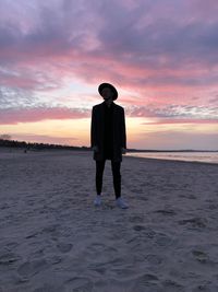 Rear view of man standing on beach against sky during sunset