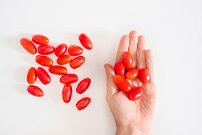 Close-up of hand holding tomatoes over white background