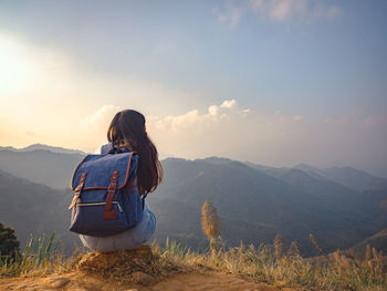 Backside of woman with backpack sitting to enjoy on mountains peak in the morning