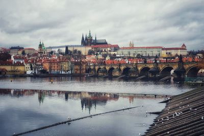 Bridge over river by buildings in city against sky