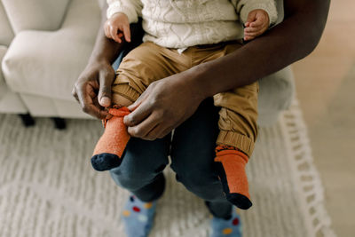 High angle view of father putting on sock to son in living room at home