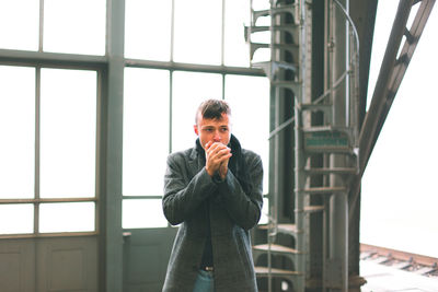 Portrait of young man standing against window