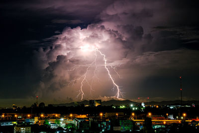 Lightning over illuminated cityscape against dramatic sky