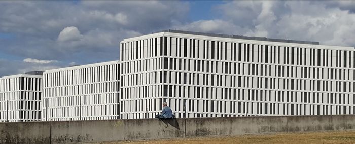 Rear view of man standing by modern building against sky