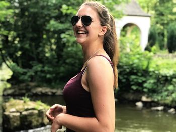 Smiling woman wearing sunglasses while standing at lakeshore