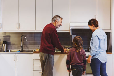 Senior man preparing food with great grandson and daughter in kitchen