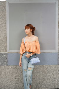 Thoughtful woman standing against gray wall